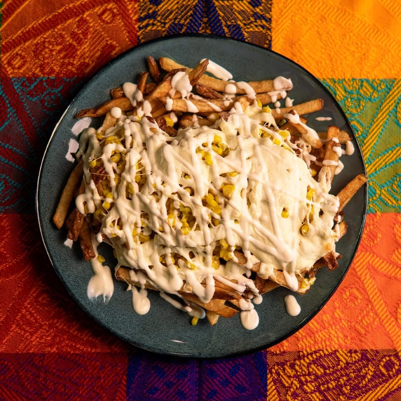 A plate of golden fries topped with melted white cheese, corn kernels, and a creamy white sauce.