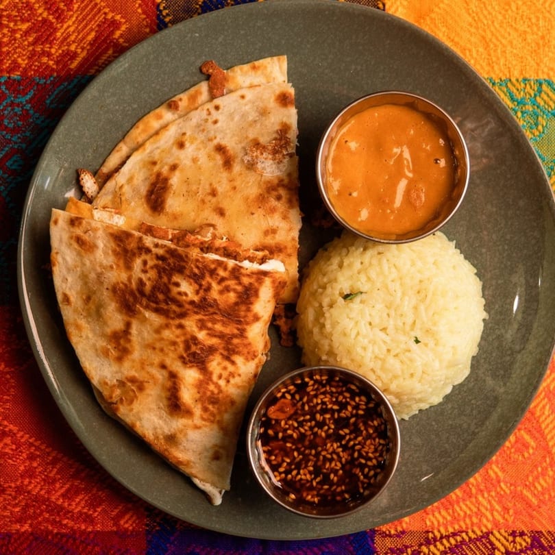 A plate of quesadillas, rice, and two dipping sauces on a colorful tablecloth.