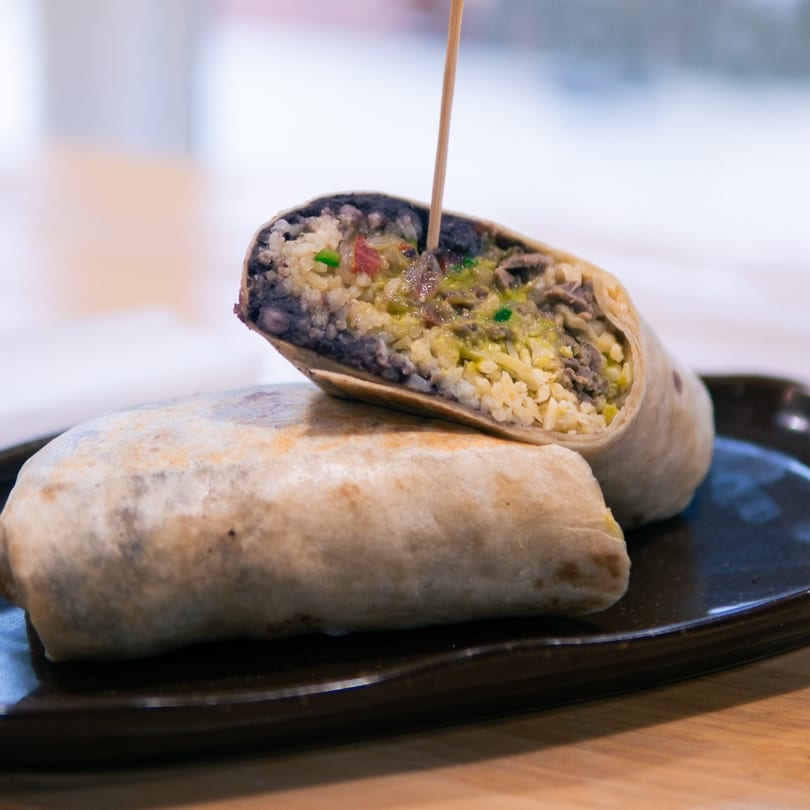 Two burritos on a black plate, one cut in half revealing rice, beans, and meat.